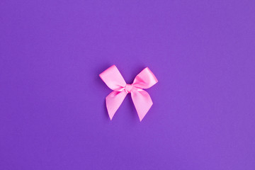 Pink bow in the center of  the violet background. Top view. Copy space. Holiday background.