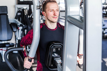  A sporty muscular man in red and black blouse, engaged in a simulator.