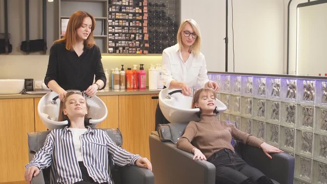 Young caucasian girls enjoy and relax with closed eyes while professional stylists hairdressers wash their heads after successful dyeing in beauty saloon