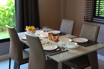 dish ware sets arrange on dining table inside eating room of modern home interior with green garden outside view the window