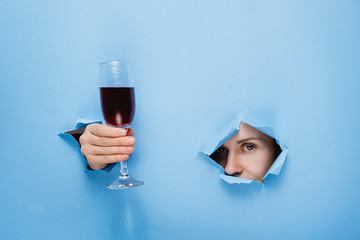 close-up of female nose and eyes keeps in his hand a glass of red wine through torn hole in blue...