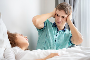 Caucasian couple in pajamas snoring and bad sleeping on the bedroom.His blocking ears with hands.