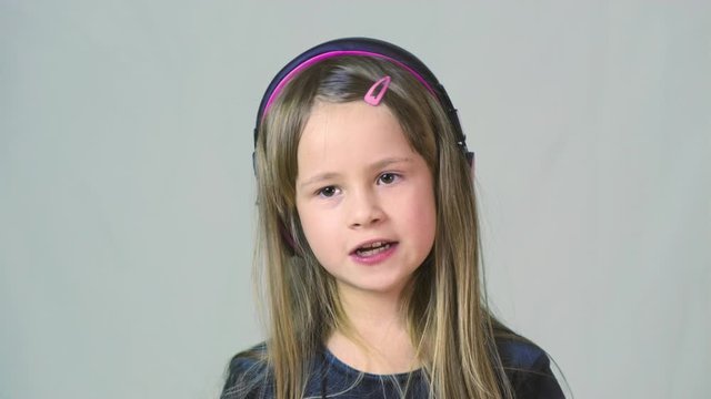 Pretty smiling cild girl listening to music in big pink earphones.