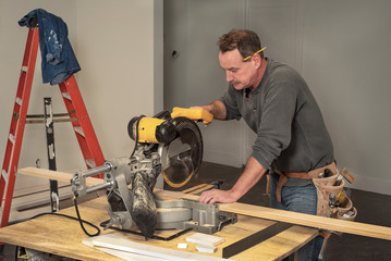 carpenter with toolbelt cuttring wood boards with electric chop saw at saw horses during home...