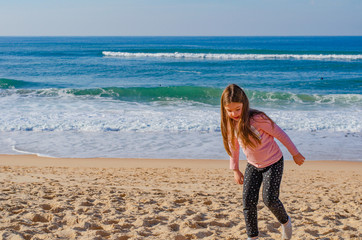 Child playing in the sand on a beach by the Atlantic ocean. Girl smiling.
