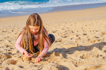 Child playing in the sand on a beach by the Atlantic ocean. Girl looking in the sand.