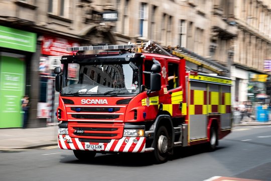 A red Scania P280 fire truck in the streets of Glasgow driving very quickly with a strong motion blur effect with focus on Scania logo