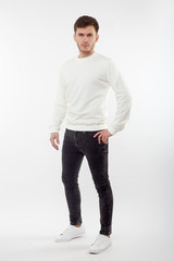 Fototapeta premium Young european man in white sweater and black pants posing on white background. Isolated.