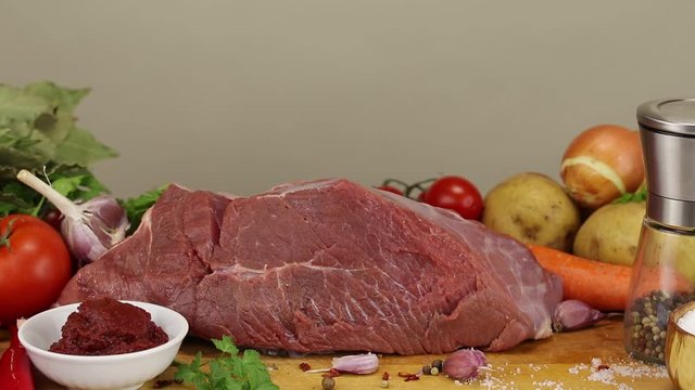 A large piece of beef meat and vegetables lies on a cutting board, close-up