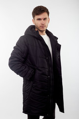 Young european man in white sweater and black pants, black down jacket posing on white background. Isolated.