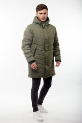 Fototapeta premium Young european man in white sweater and black pants, olive down jacket posing on white background. Isolated.