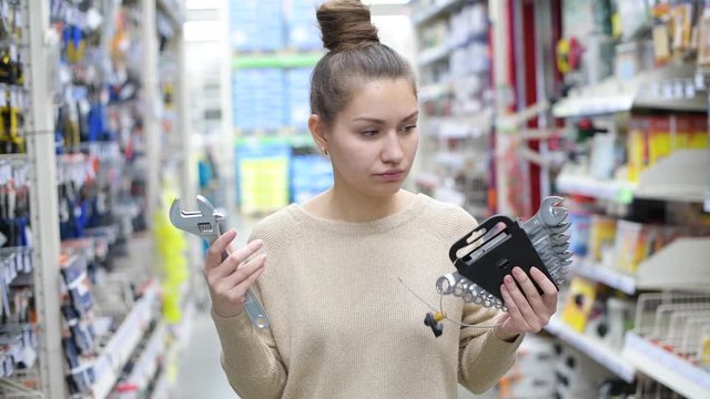 young woman chooses a work tool in a hardware store. A girl chooses between a set of wrenches and an adjustable wrench