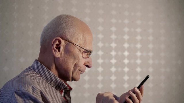 senior man in glasses discovers smartphone abilities touching display with finger standing against wallpapers closeup