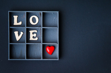 vintage wooden box with white letters creating romantic  love word and red heart over black...