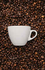 Fototapeta premium white coffee cup lies in roasted coffee beans of the highest standard