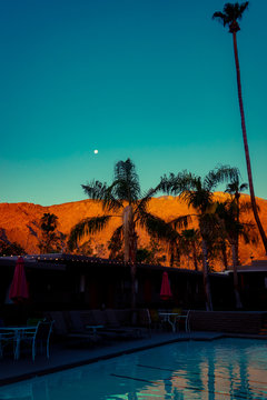 Swimming Pool String Lights and Palm Trees in the Foreground of Red Desert Mountains and Moon at Night Near Palm Springs California