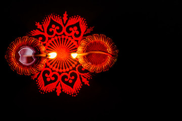 Two glowing terracotta lamps and rangoli against dark background. diwali concpet