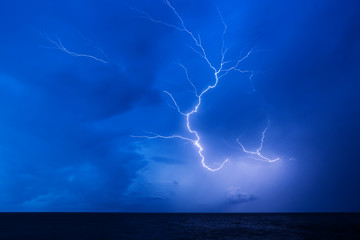 Powerful lightning in the blue sky over the dark sea