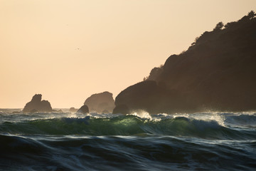 Green sea waves at sunset in front of the stone cape