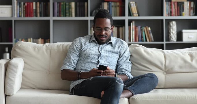African man sitting on couch using smart phone at home