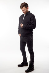 Young european man in white sweater and black pants, black bomber jacket posing on white...