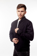 Young european man in white sweater and black pants, black bomber jacket posing on white...