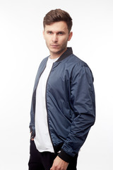 Young european man in white sweater and black pants, blue bomber jacket posing on white background. Isolated.