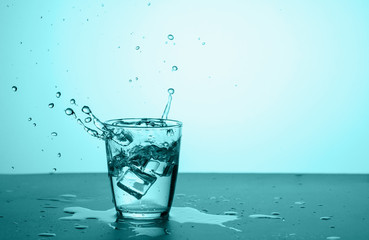 Glass of water with splash and ice on turquoise background