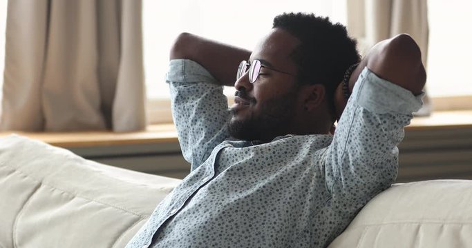 Calm african young man rest on comfortable couch enjoying wellbeing