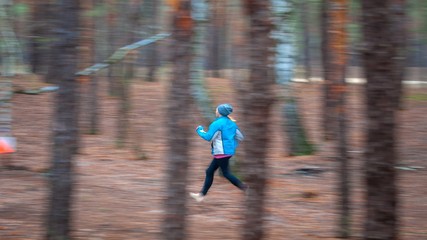 Orienteering. Motion blur. Motion blur. A young girl athlete with a sports card in his hand quickly runs along the distance of orienteering in the autumn forest, approaching a control point. Concept.