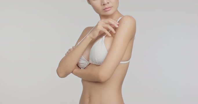 Bikini model touching her chest looking sexy in white background, look up shot. Asian woman in white bikini.