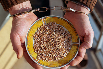 Male with handcuffs holding plate with raw grits. Part of hard life concept.