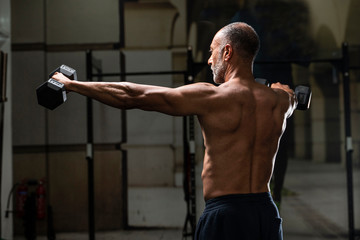 Backward view of a muscular shirtless mature older bodybuilding athlete with balding gray hair does...