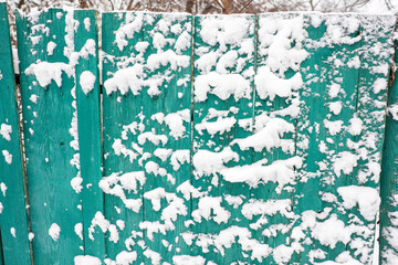 Snow-covered blue old rural wooden fence. Winter in the village. Snow and icicles are everywhere. New Year and Christmas mood. Severe frost. Ice in the puddles. Slippery roads.