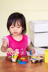 Vertical Portrait image of​ Asian baby​ girl​ playing​ the​ wooden​ block toys.​ On​ wooden​ table.​ 1-2​ years​ old​ of​ child.​ Learning​ and​ development​ of​ kid​ concept. With copy space.