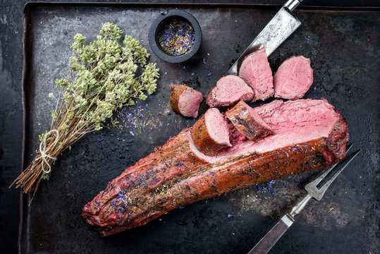 Gegrilltes dry aged Hirschfilet St&uuml;ck mit Medaillon Steak natur mit Kr&auml;utern und Preiselbeer Sauce angeboten als Draufsicht auf einem rustikalen Metall Tablett