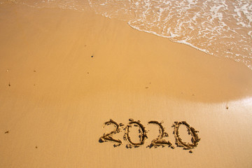 Summer beach holiday 2020 season golden sand - year - decade - new season lettering on the beach with wave and clear blue sea. Numbers 2020 year on the sea shore, message handwritten New Years concept
