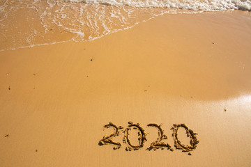 Summer beach holiday 2020 season golden sand - year - decade - new season lettering on the beach with wave and clear blue sea. Numbers 2020 year on the sea shore, message handwritten New Years concept