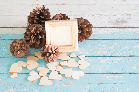Wooden picture frame placed on a vintage wooden table with Brown Pinecone or Conifer cone and wooden heart decoration