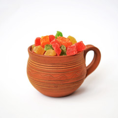 Assorted candied fruit in a clay pot on a white background
