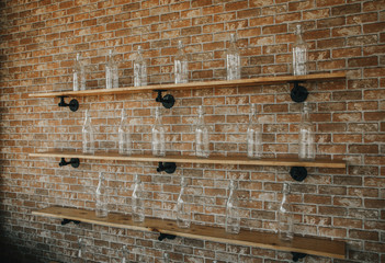 Vintage style clear glass bottles are lined up on bare wooden shelves, showing the wood texture to...