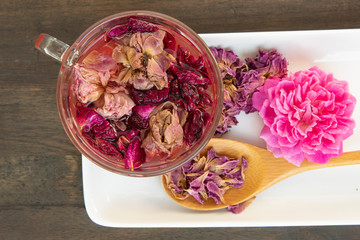 dried pink roses and tea in glass on black wood background, dry rose petala in wood spoon