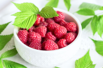 ripe raspberries in a white ceramic bowl close-up. background with raspberry berries and leaves.