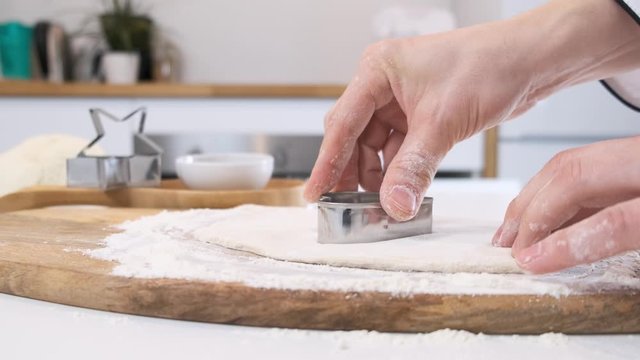 Female hands cutting out shapes from rolled dough with heart cutters on white table. Close up.