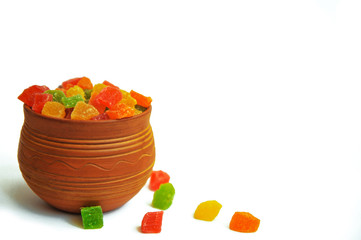 Assorted candied fruit in a clay pot on a white background