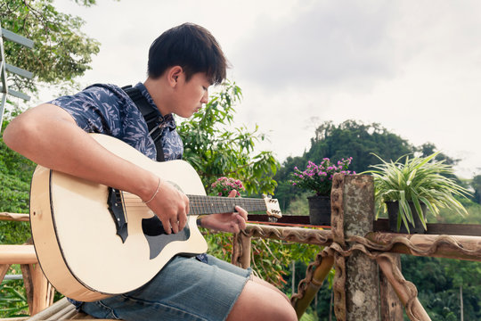 A young Asian man is playing the guitar on the balcony.
