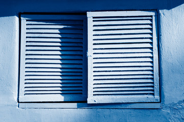 Old closed window with classic blue shutters on a blue wall background