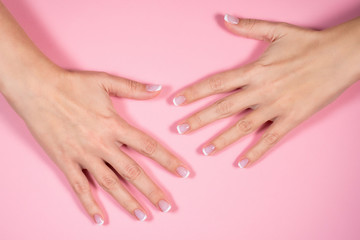Obraz na płótnie Canvas Closeup top view of two beautiful female hands with fresh professional french pink and white manicure isolated on pastel pink background. Horizontal color flatlay photography.