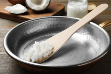 Frying pan with coconut oil and wooden spatula on wooden table, closeup. Healthy cooking