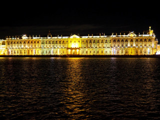 building facade illuminated by yellow lights reflecting in the water of a wide river at night